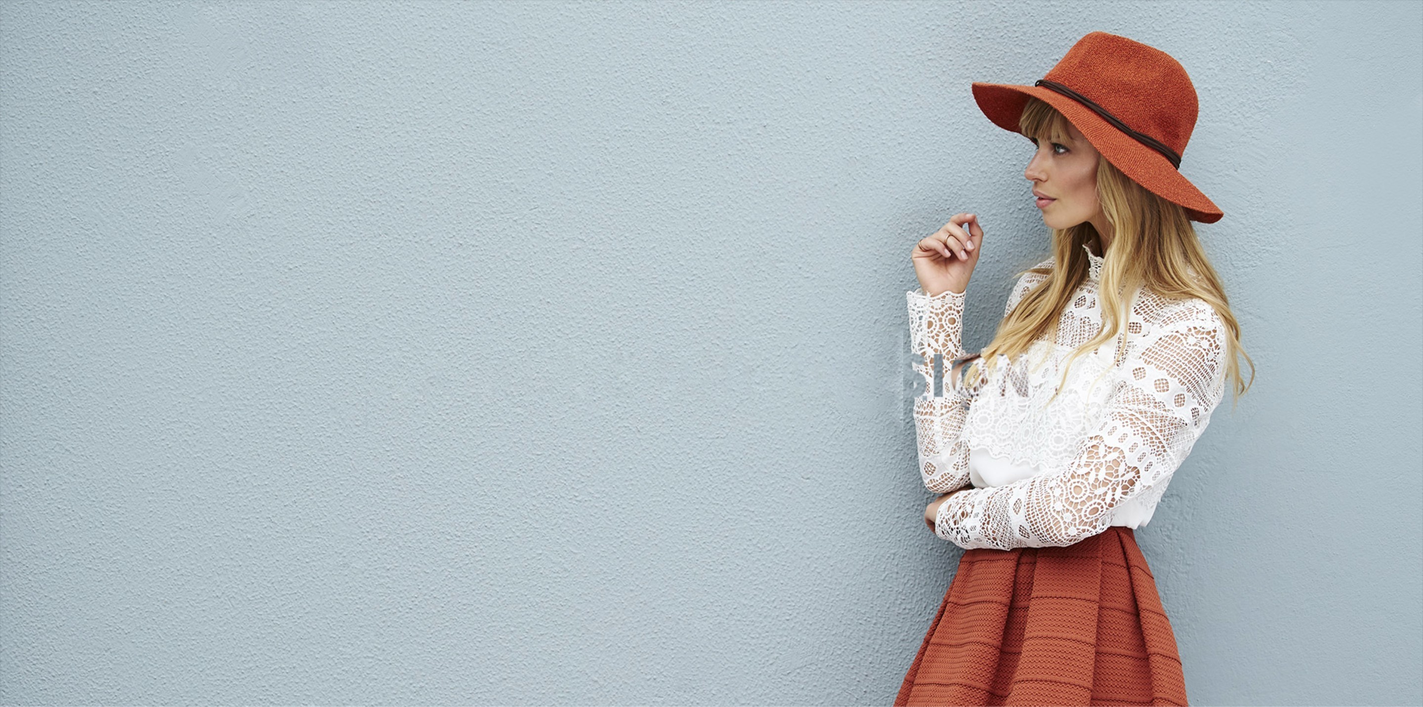 Femme portant un chapeau feutre et une blouse en dentelle devant un mur bleu