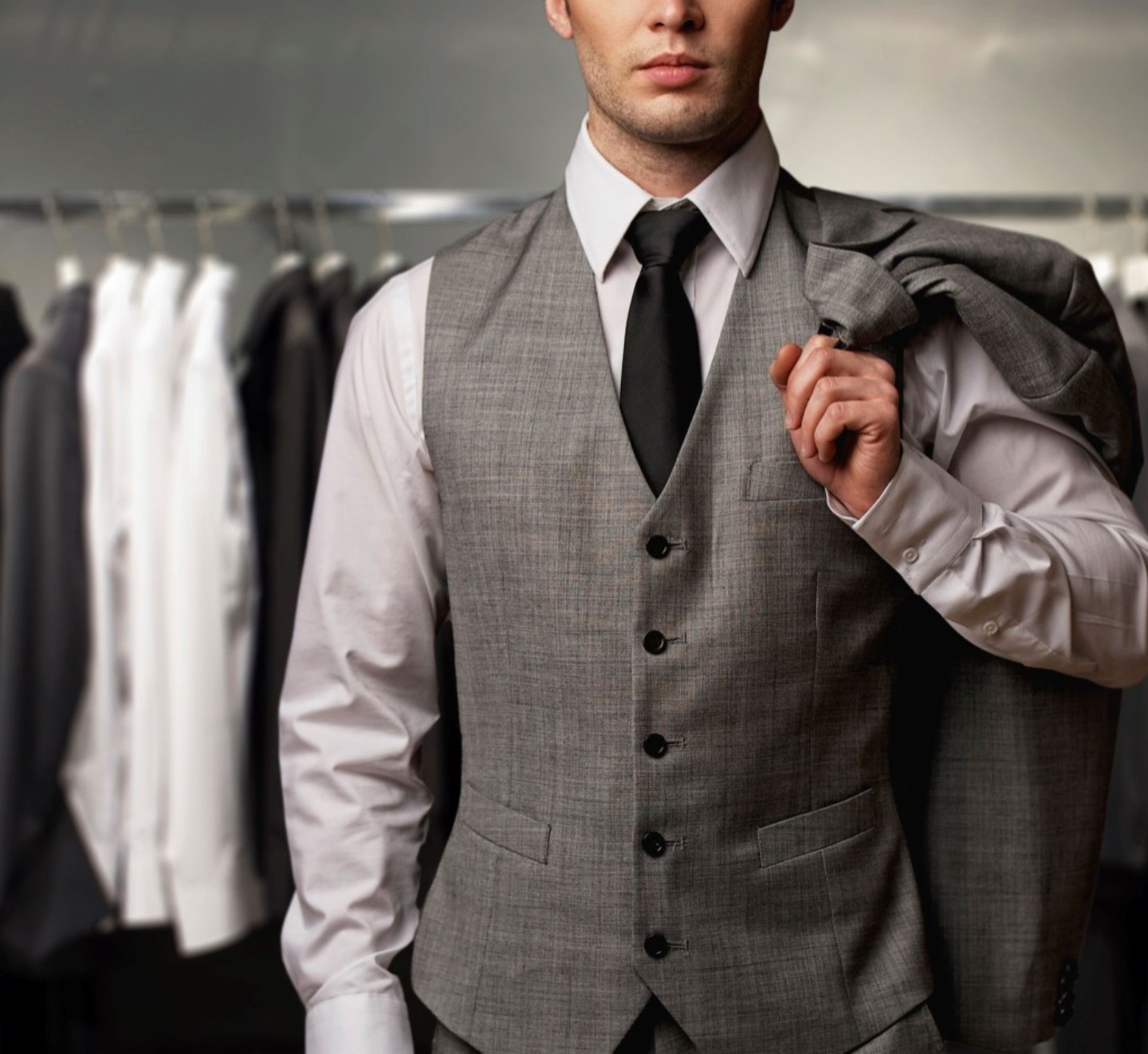 Homme en gilet de complet devant un portant de chemises